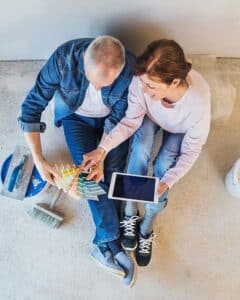 Couple selecting paint colors together, discussing plans on a tablet, related to finding a premarital therapist near me.