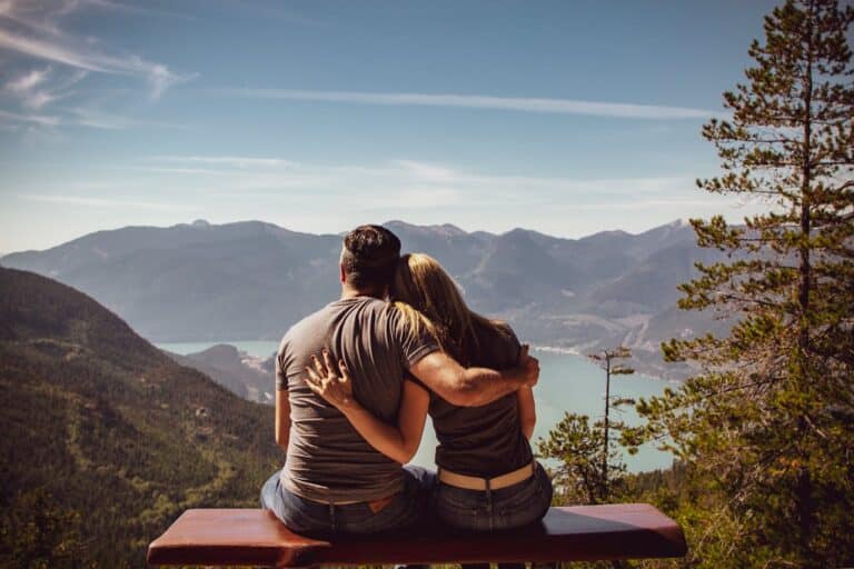 Couple sitting together on a bench overlooking mountains and a lake, symbolizing emotional connection in relationships.