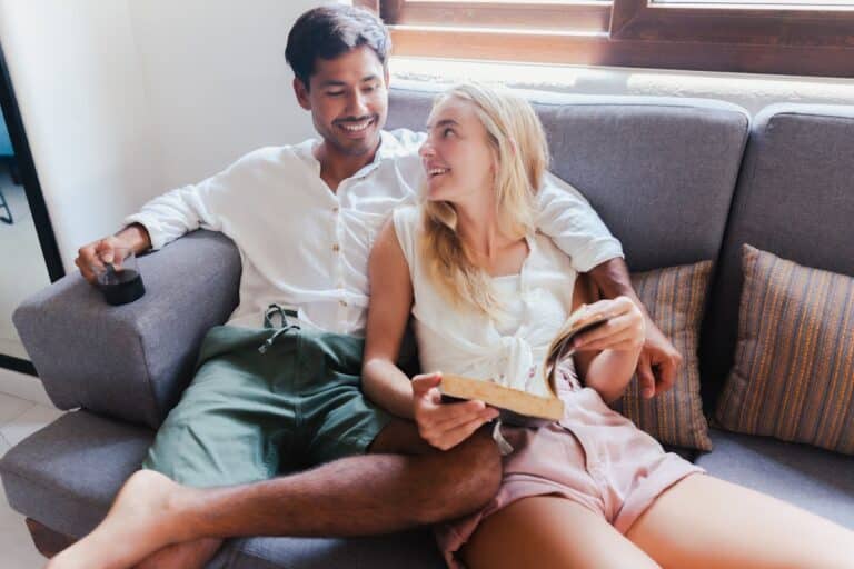 Smiling couple relaxing on a couch, talking and reading together after de-escalating a conflict at home.