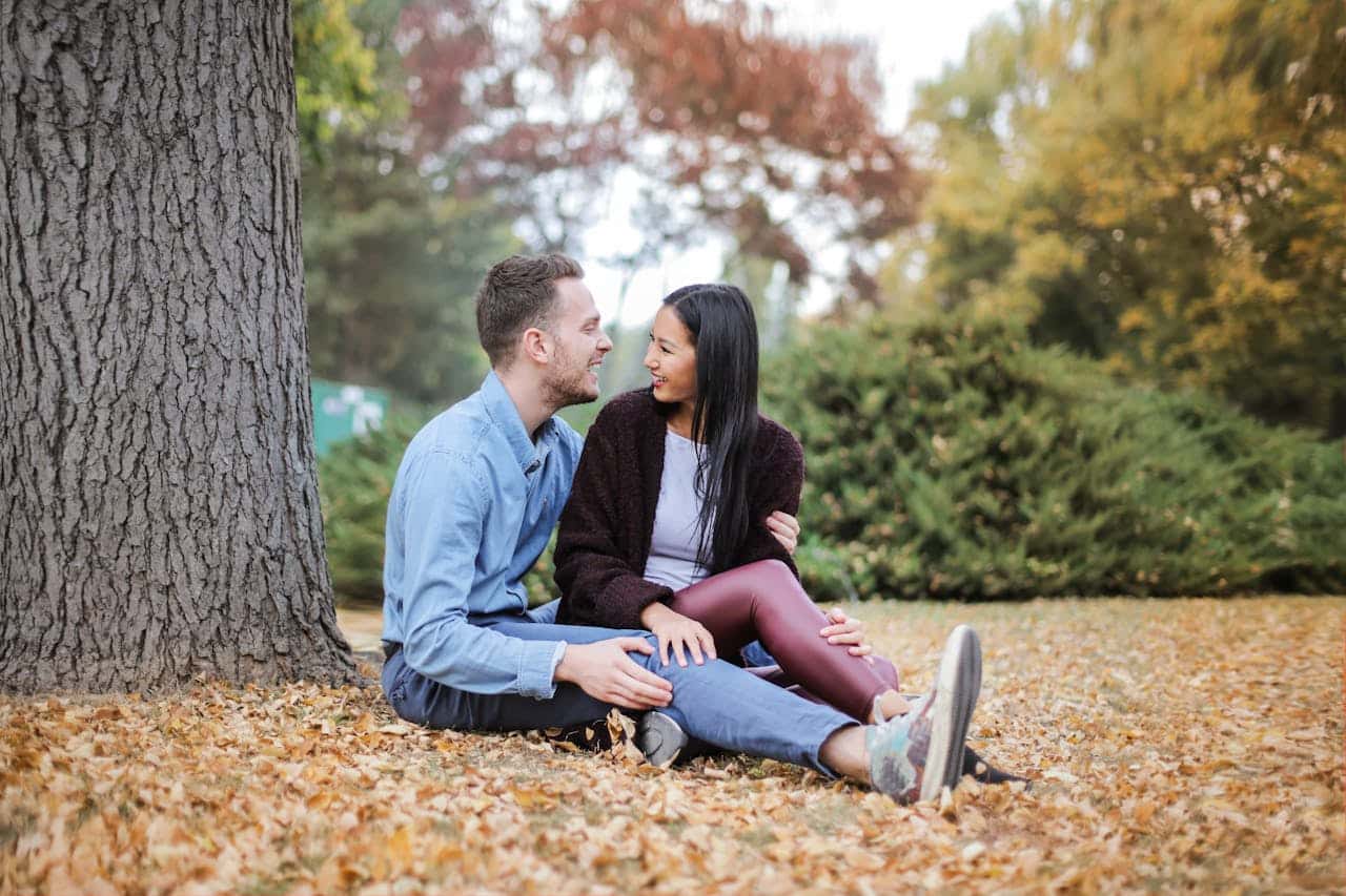 Couple sitting on autumn leaves outside, smiling and talking together