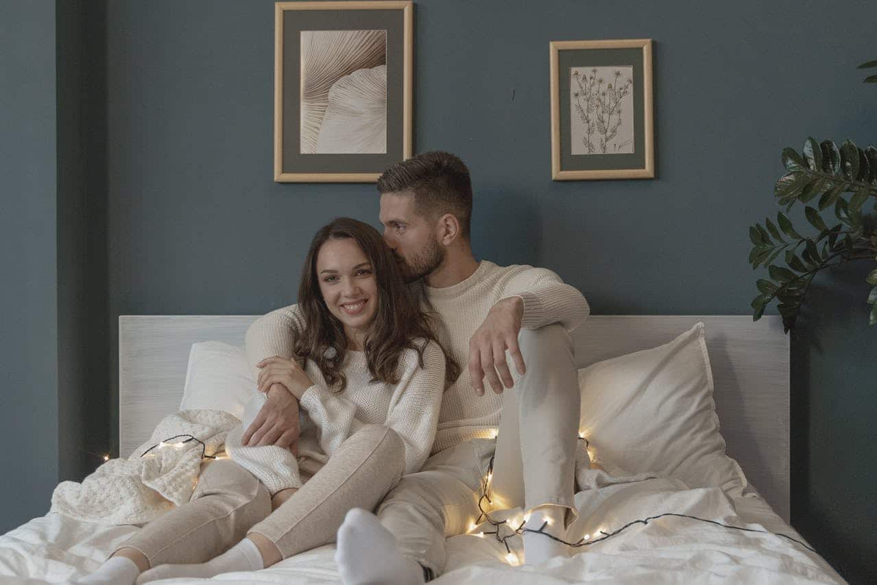 Couple sitting close on a bed with warm lights, sharing a calm, affectionate moment after resolving an argument at home.