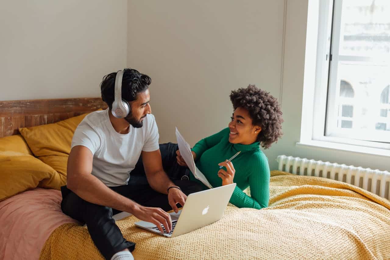 Couple talking and smiling while working on a laptop at home, representing healthy communication in relationships.