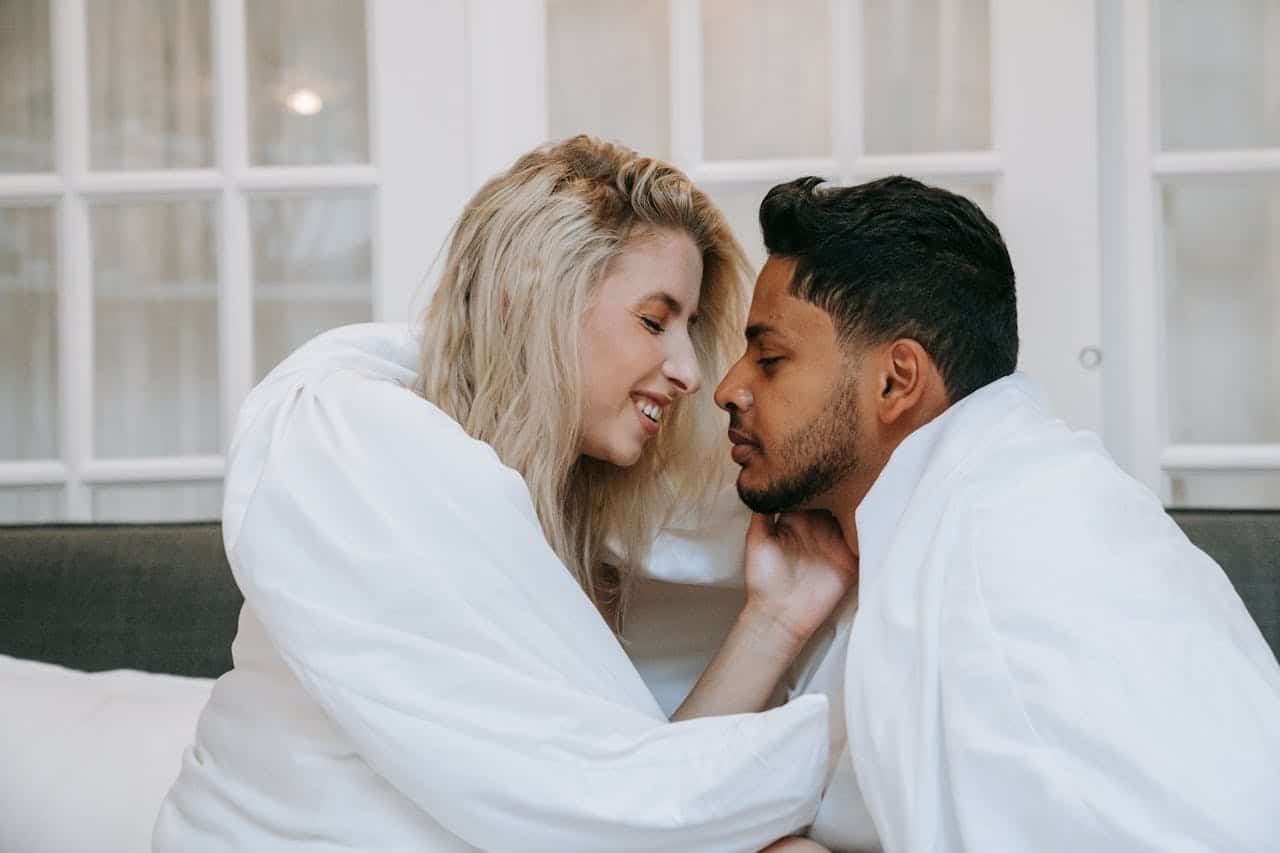 Smiling couple maintaining eye contact and gentle touch symbolizing trust, communication, and emotional intimacy explored during sex therapy sessions.